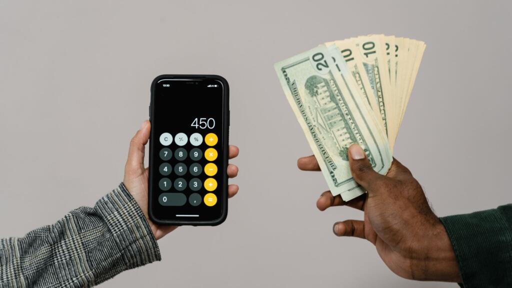une main tendue à gauche tient une calculatrice et une main tendue à droite tient des billets de banque