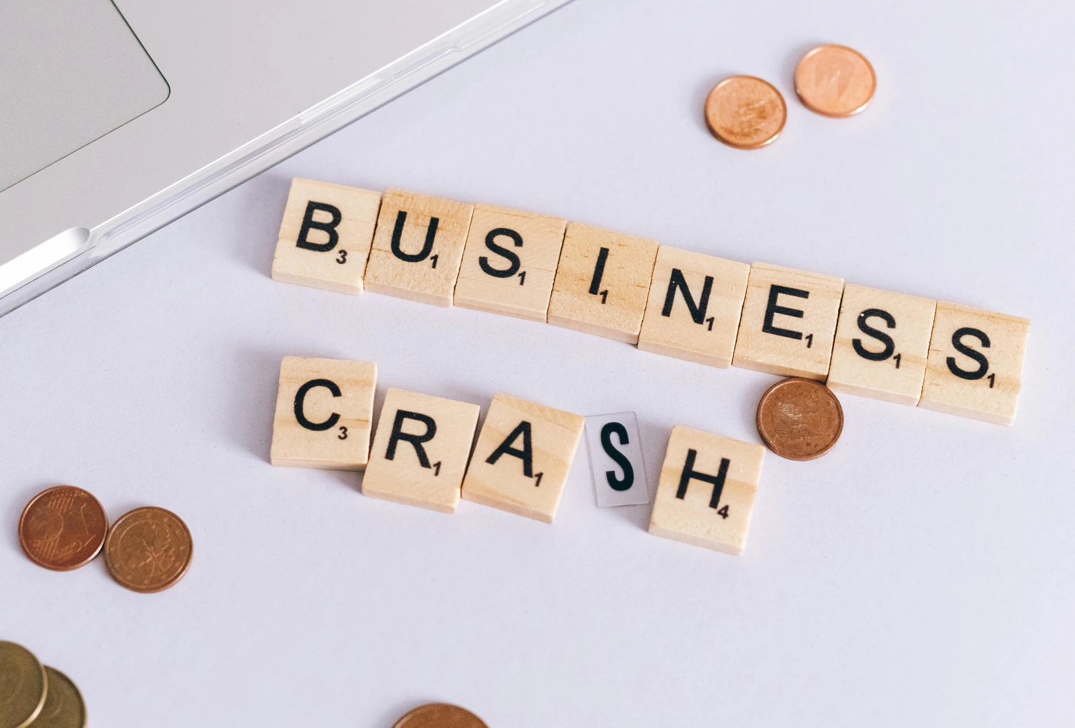 Lettres en bois formant les mots « Business Crash » avec des pièces de monnaie, illustrant les pertes financières causées par une mauvaise maintenance informatique.